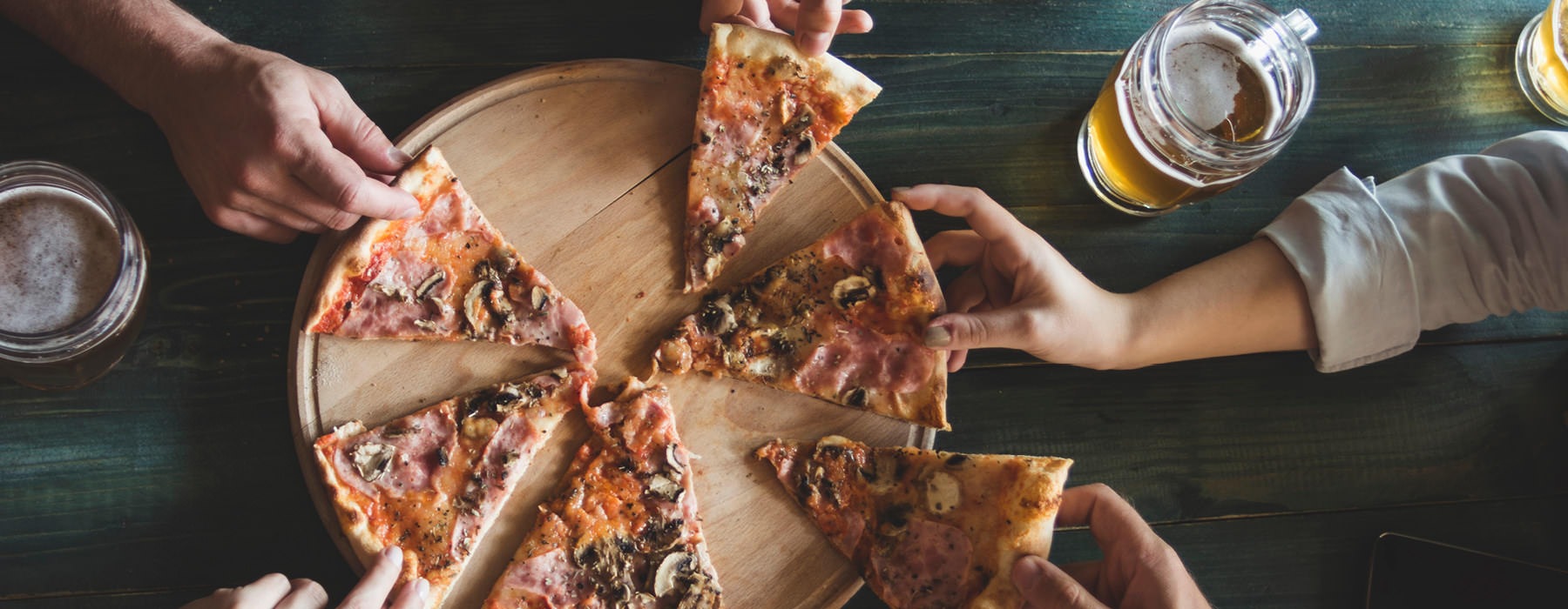 hands reach in for slices for pizza in local restaurant