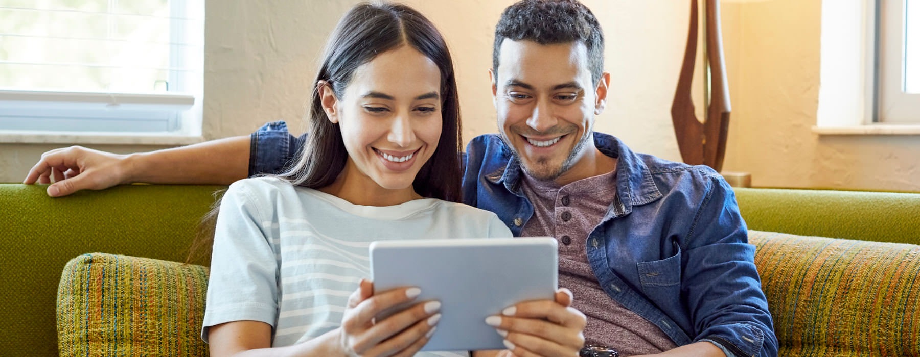 young couple looks at iPad while relaxing on their couch